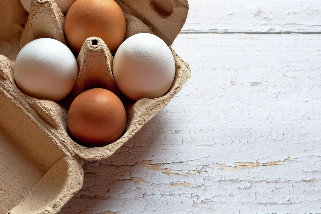 Brown and white eggs in a cardboard carton on a wooden table